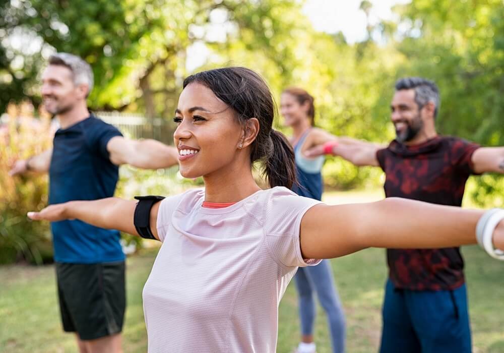 Group of multiethnic mature people stretching arms outdoor. Middle aged yoga class doing breathing exercise at park. Beautifil women and fit men doing breath exercise together with outstretched arms. 